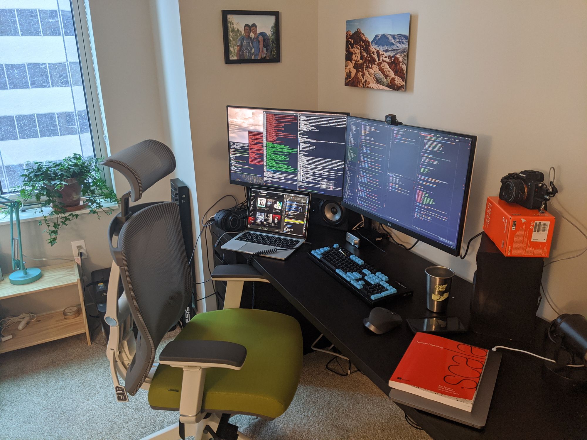 Home office with two monitors and a messy desk with a view out the window from a highrise. It is snowing.