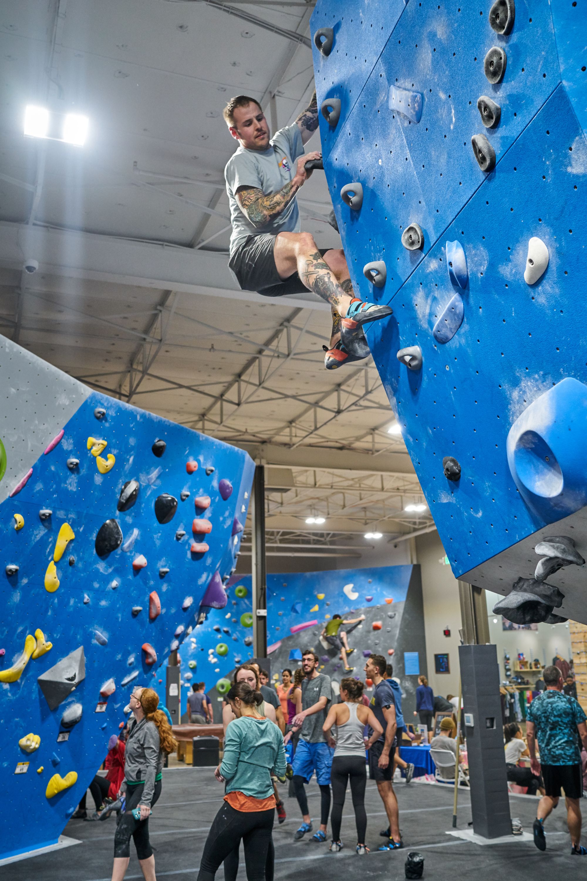 Looking up at a man bouldering in a indoor gym.