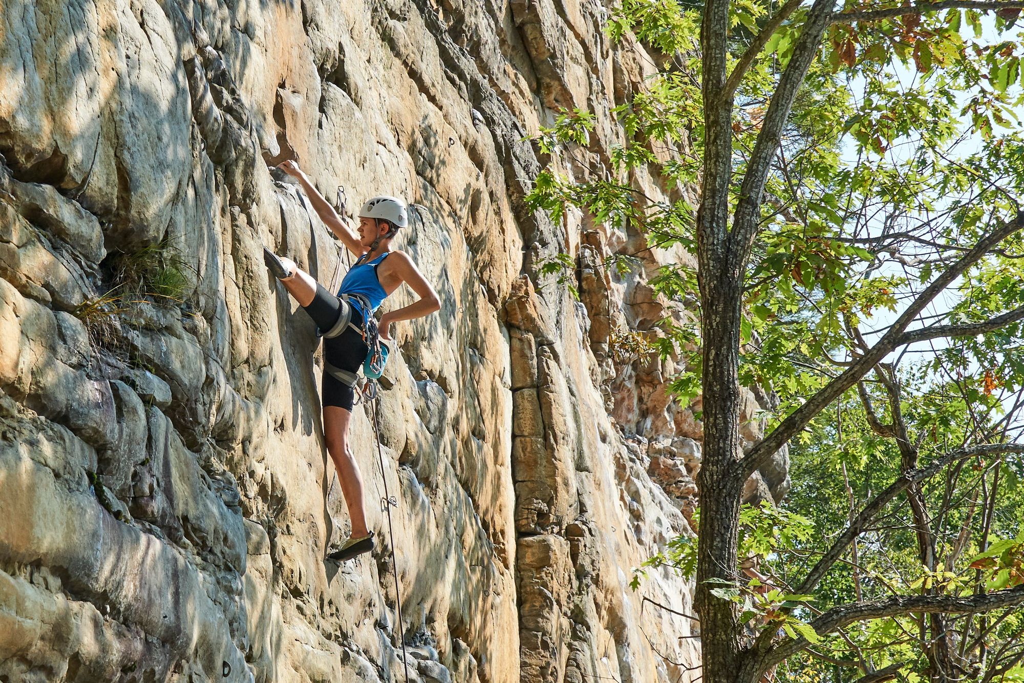 Rebecca rock climbing, hanging by one hand.