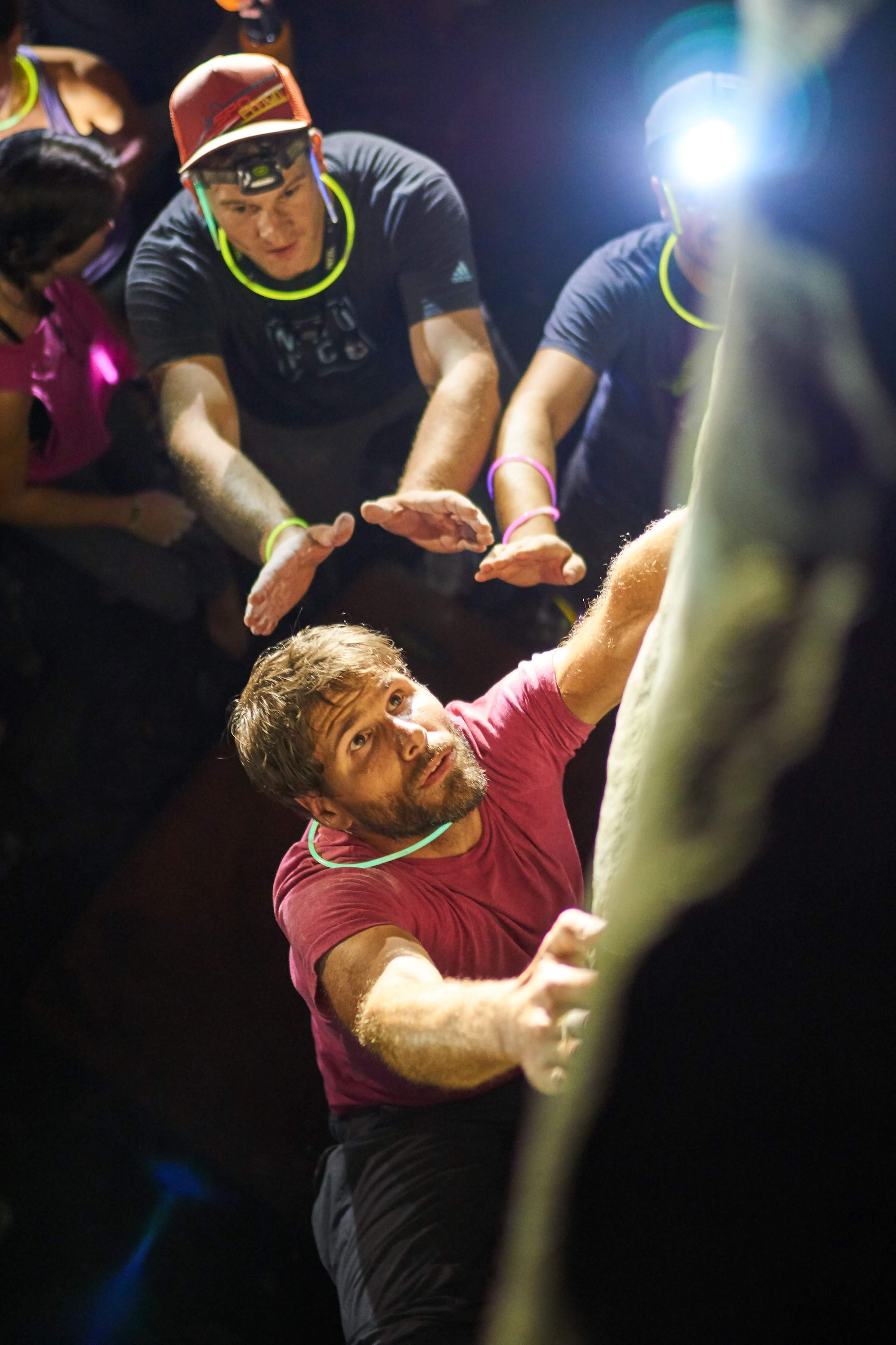 Climber low on the ground at night lit by headlamps.