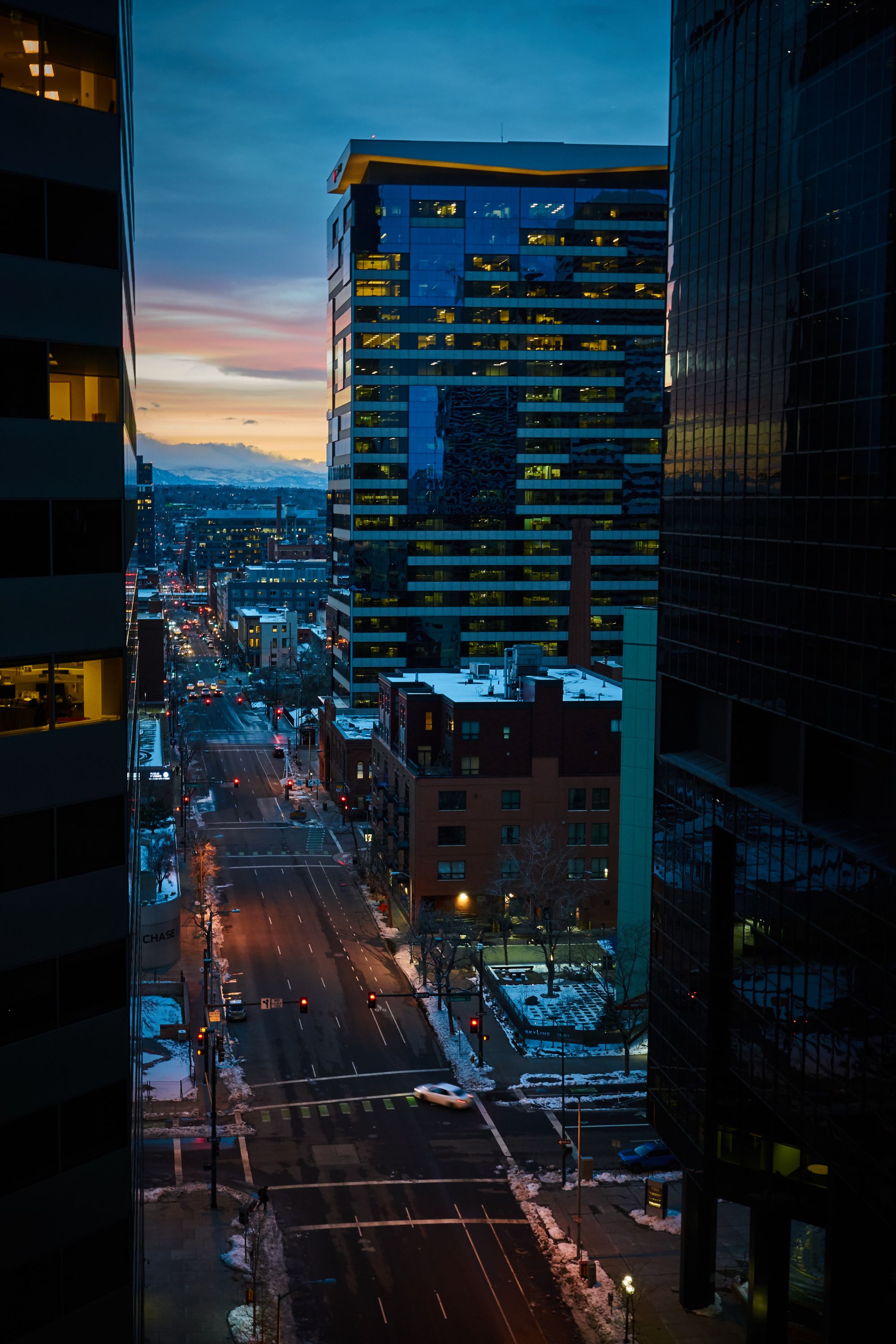 Look down denver city streets as sun is setting. You can see some mountains between the highrises.