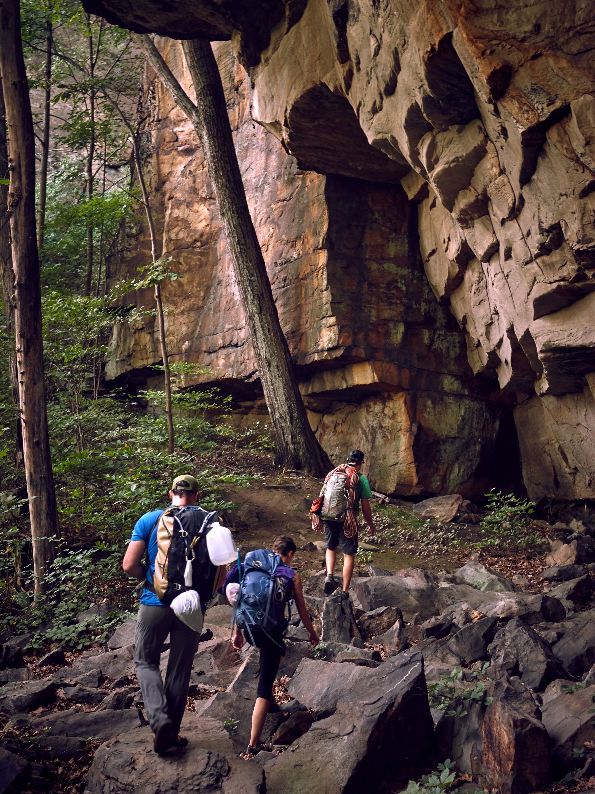 Rock climbing crew hiking out next to rocks, with rope on backpack.