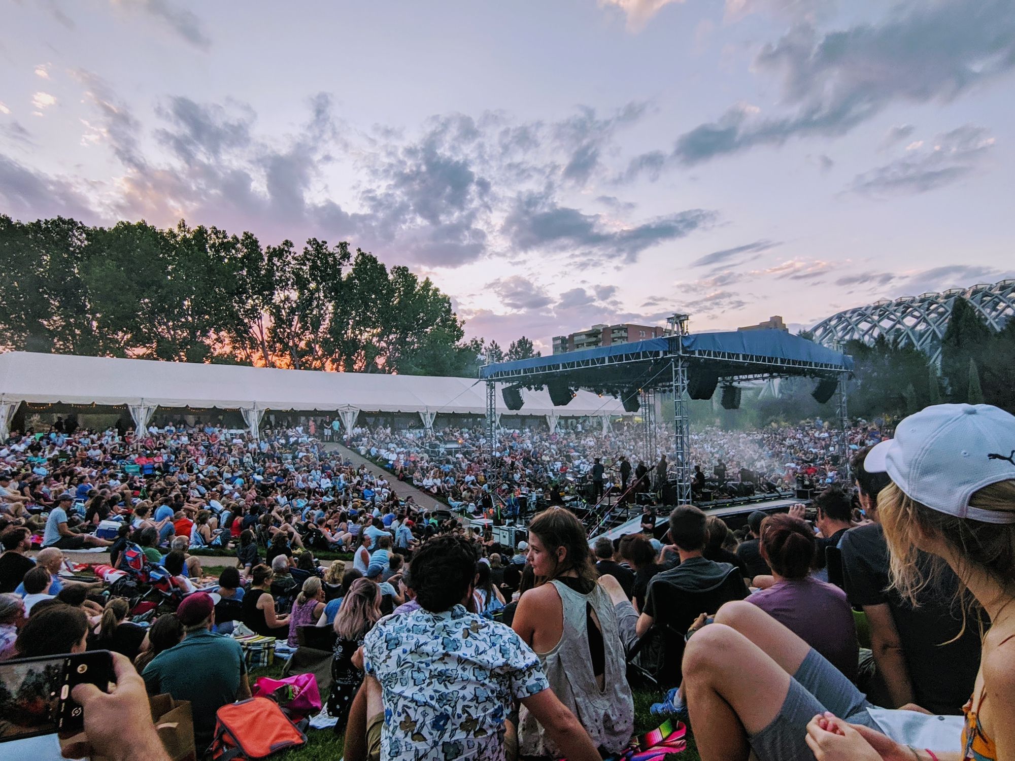 Stage in the center of a large concert crowd. Skyes are colorful as sun is setting.