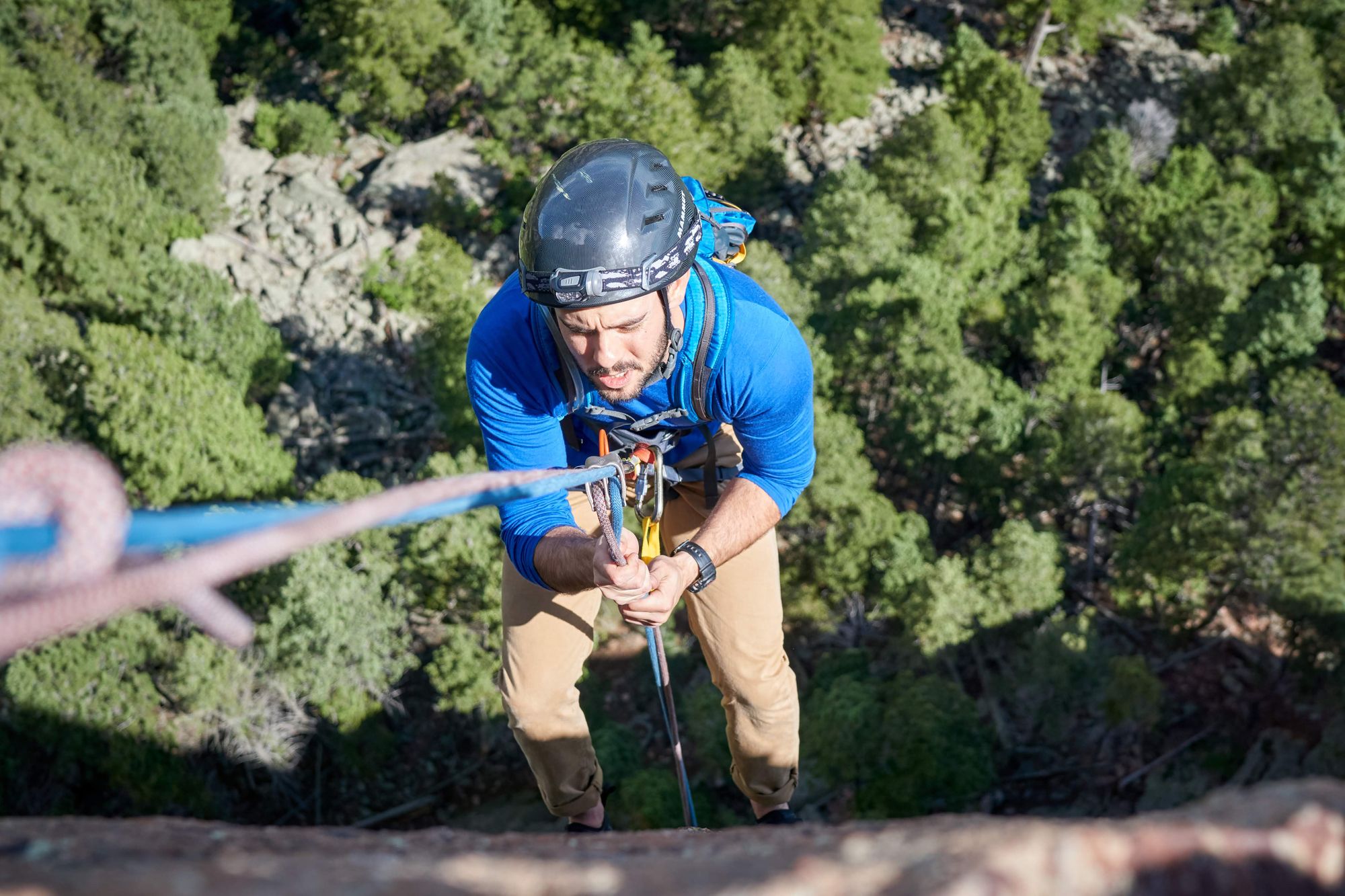 Looking down at a man rapelling, frowning, with a hundreds of feet of air below him.