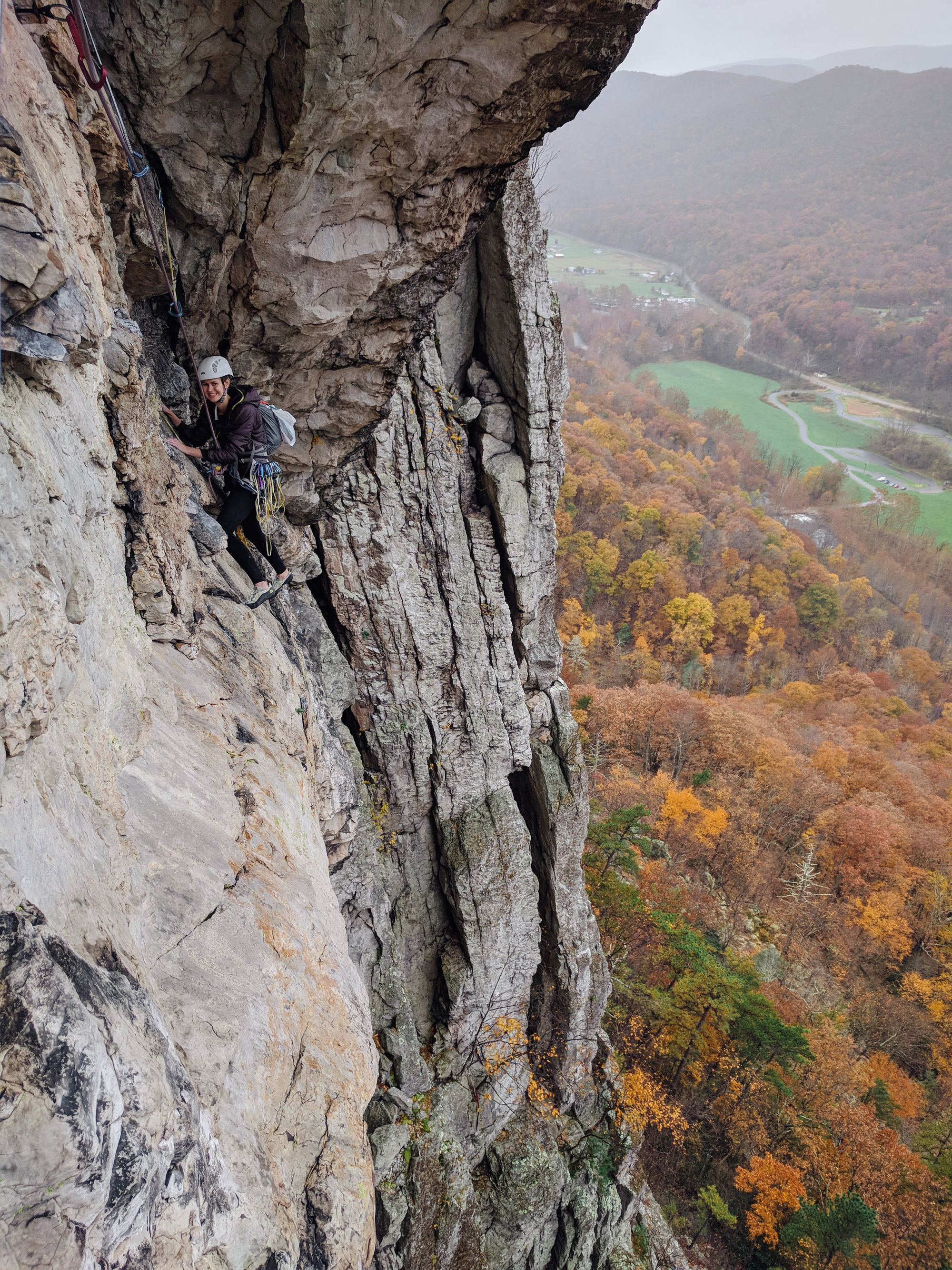 Looking down at a rock climber climbing horizontally beneath a rock roof.