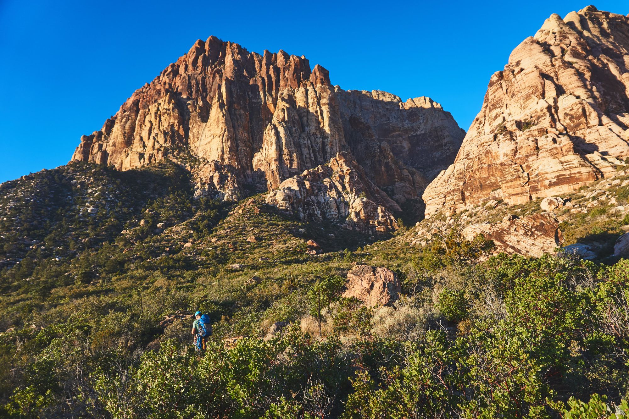 Man hiking to a large sandstone rock formation/mountain in the distance.