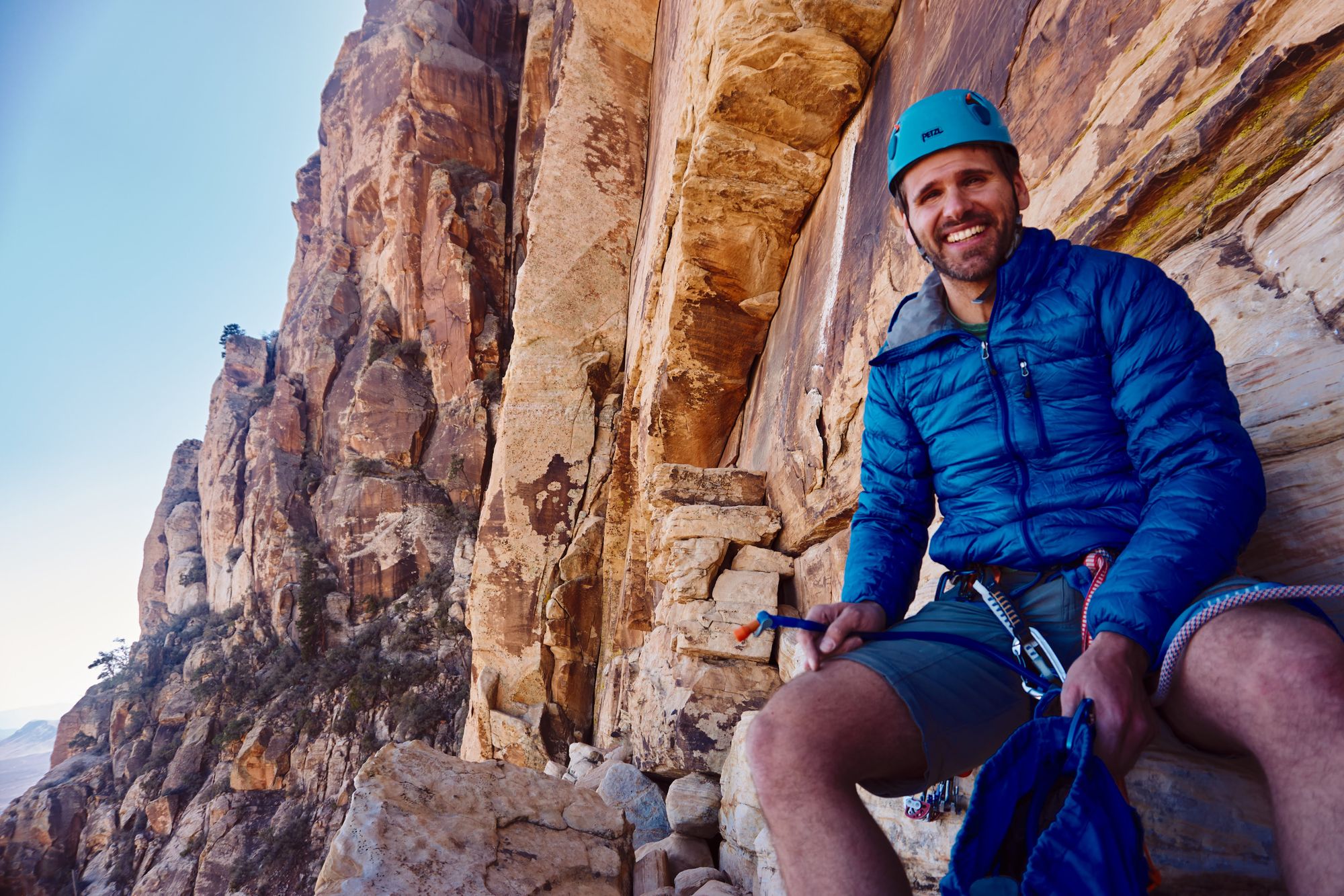 Ryan smiling, sitting in the middle of a shelf ona  rock climb.