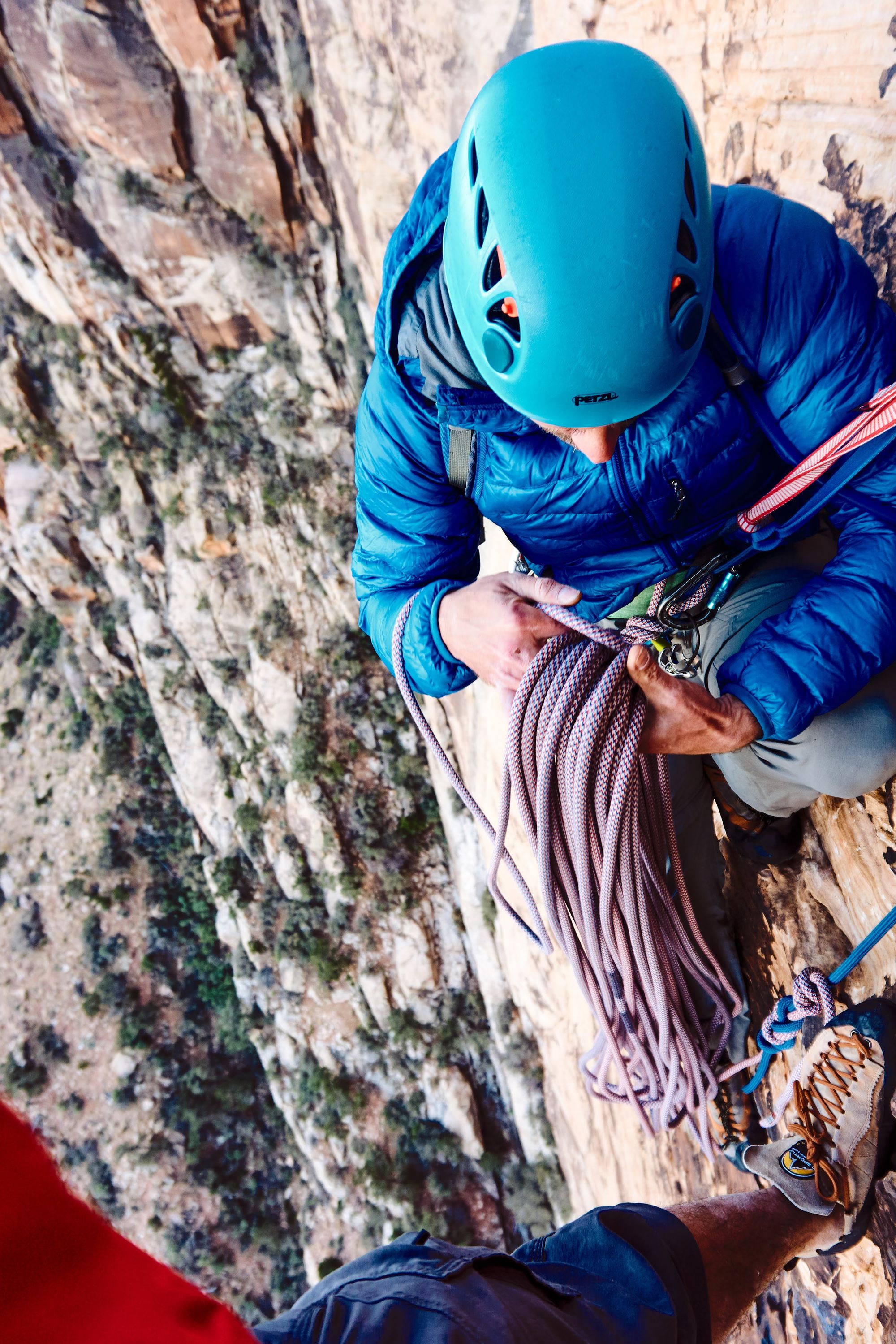 Picture of two people setting up rapelle. A coil of rope is being handled while hundreds of feet in the air.